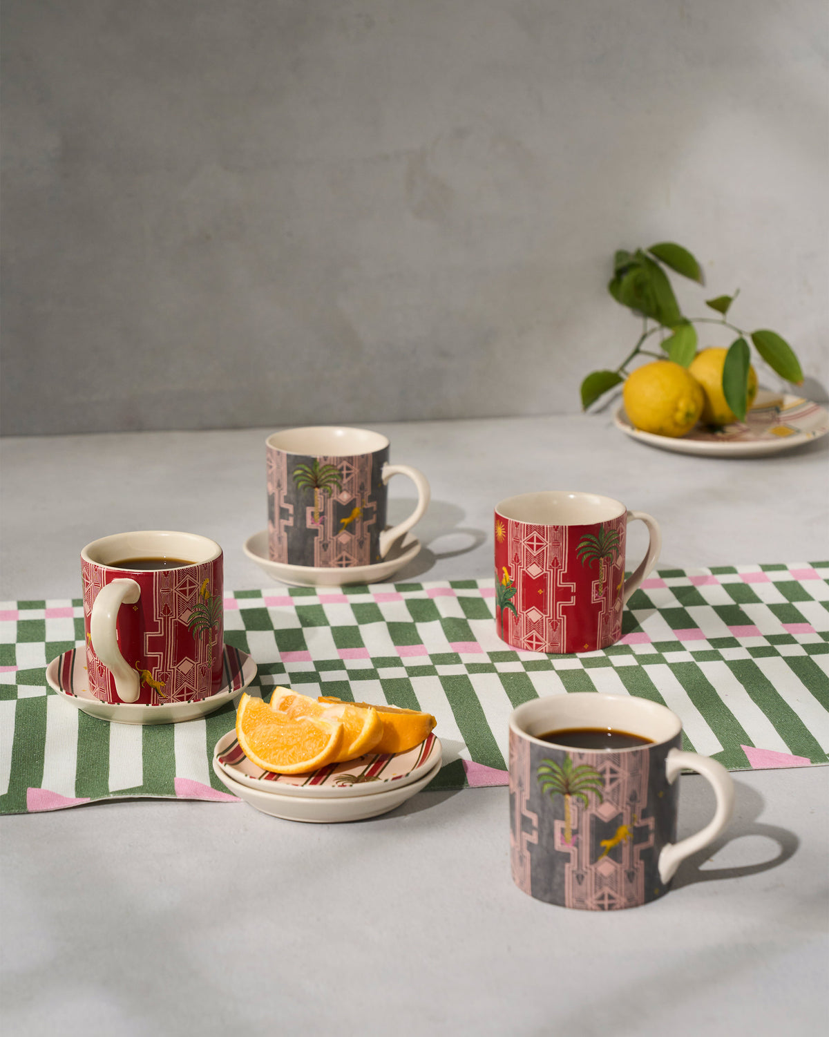 Leafy Affair mugs with palm motifs styled on a striped table runner.