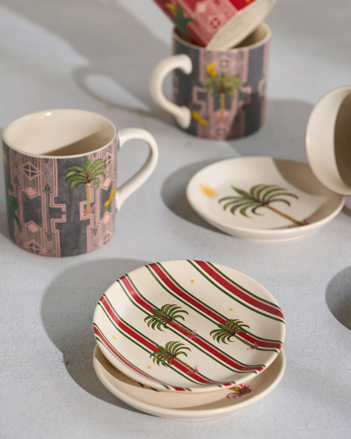 Charcoal Leafy Affair mug with palm motif beside matching tea plates.