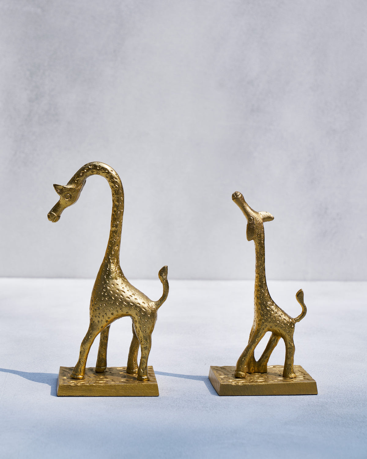 Pair of Giraffe bookends in textured gold with one neck arched down and one looking up.