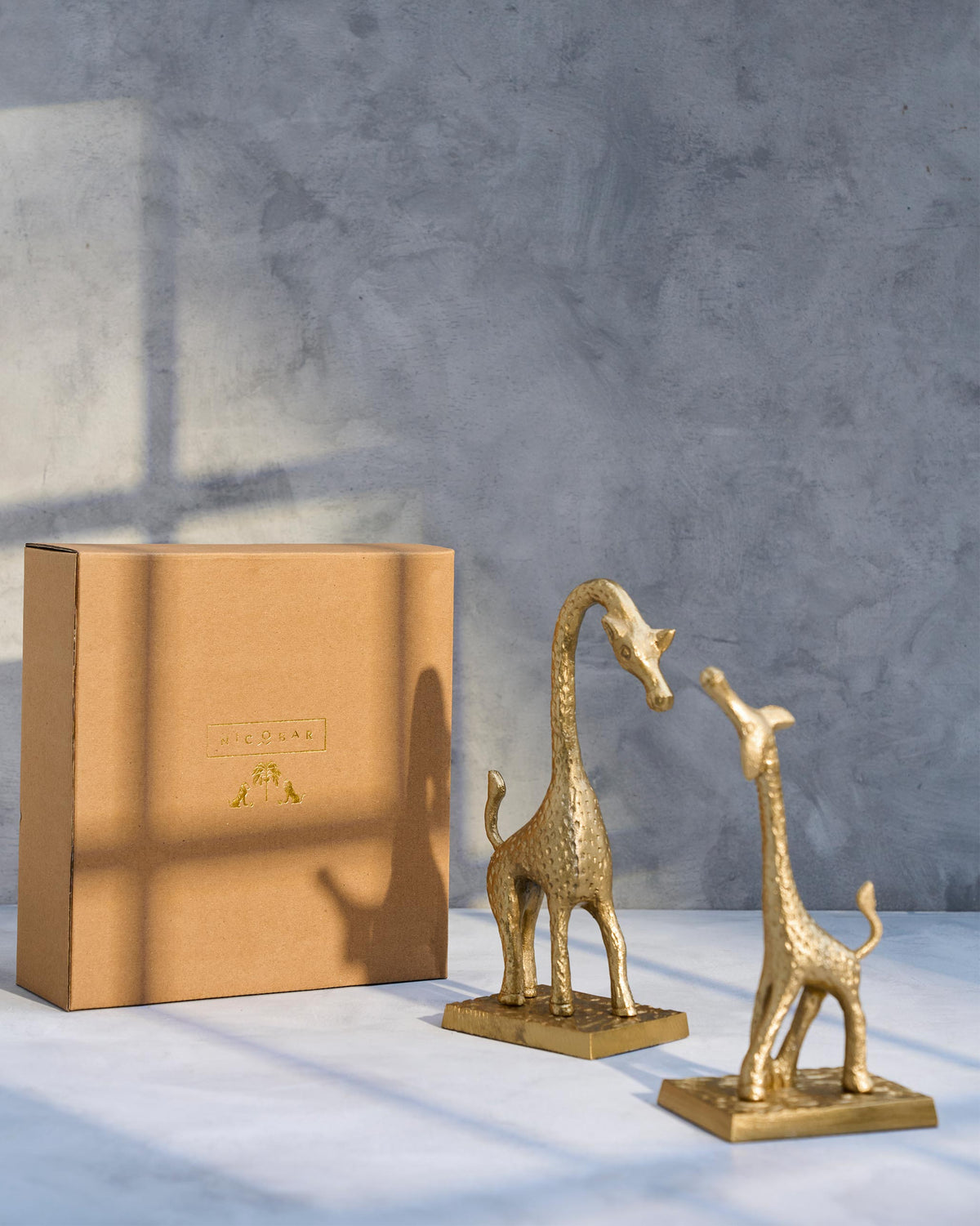 Giraffe bookends standing beside a kraft Nicobar gift box.