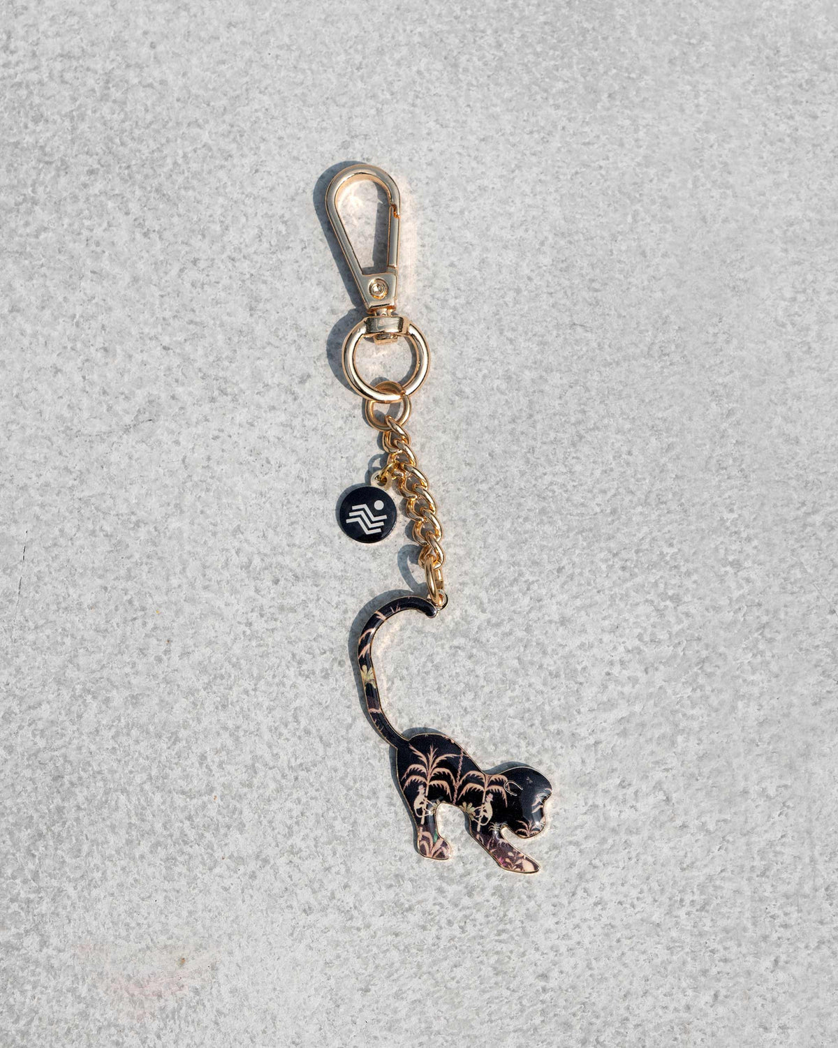 Black monkey keychain charm with gold palm motifs and a Nicobar tag.