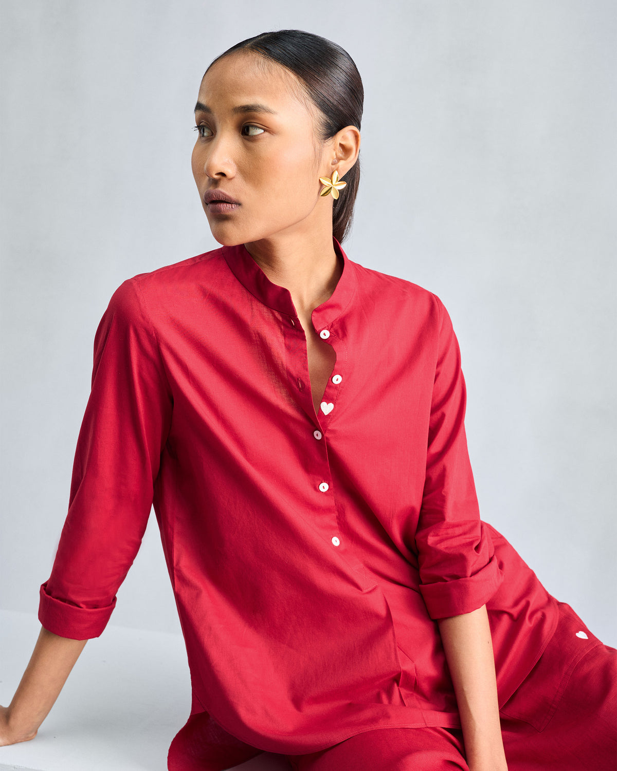 Person wearing a red mandarin collar top with a white heart button.