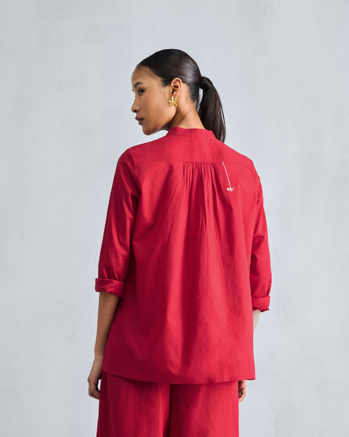 Back of a red mandarin collar top with a gathered yoke and white embroidery.