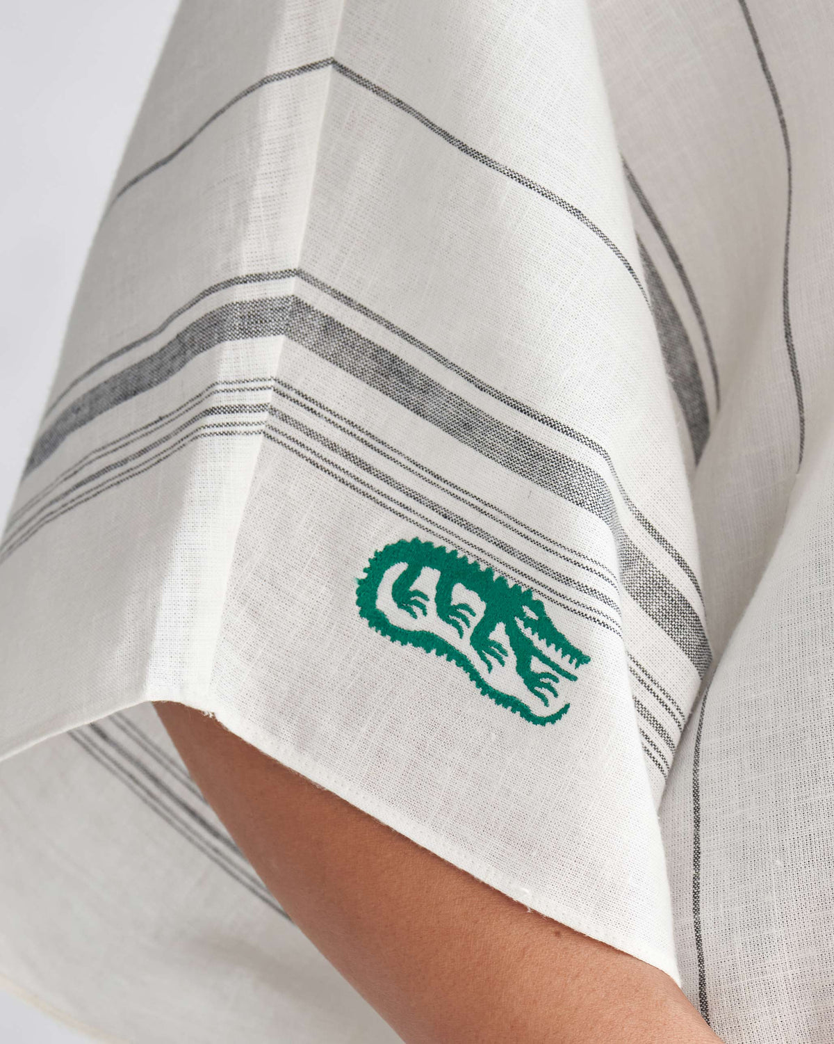 Close-up of an ivory collared kaftan sleeve with a green crocodile motif.
