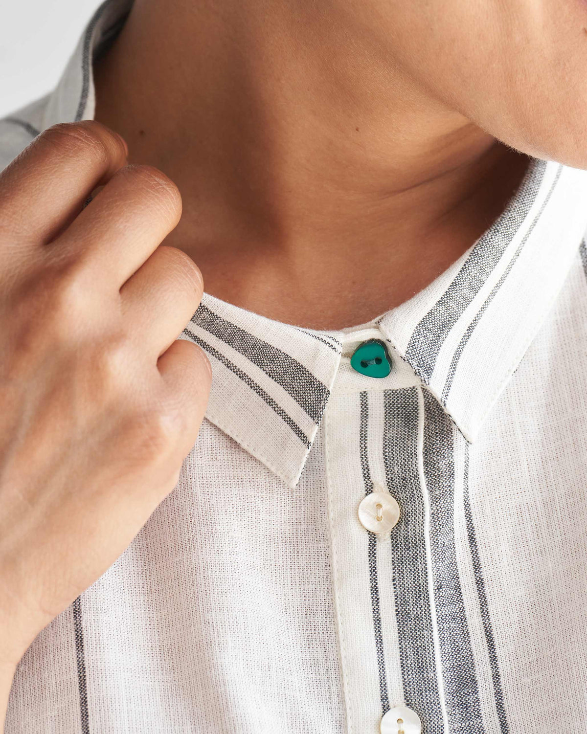 Close-up of an ivory collared kaftan neckline with a teal button.
