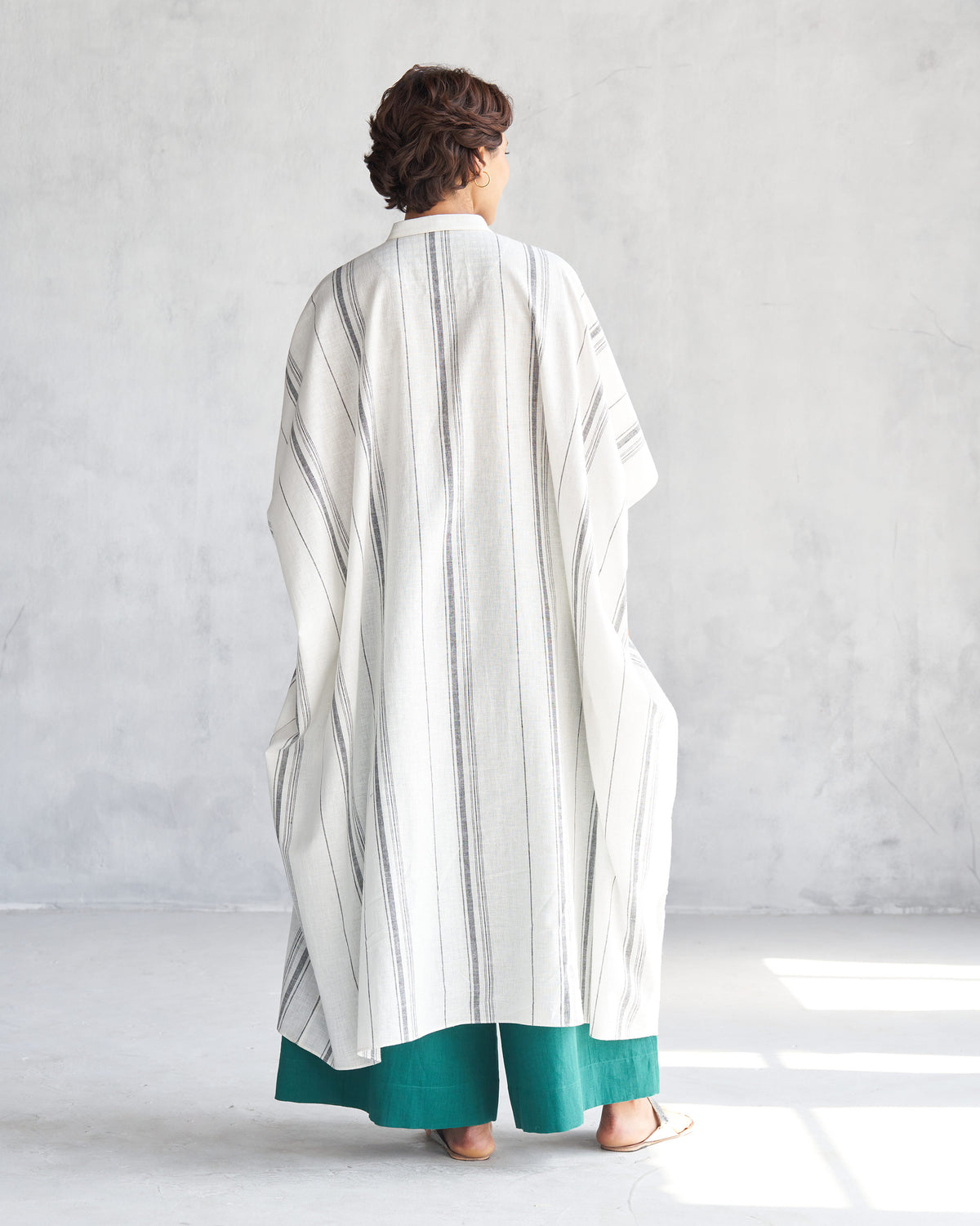 Back of an ivory collared kaftan with grey vertical stripes.