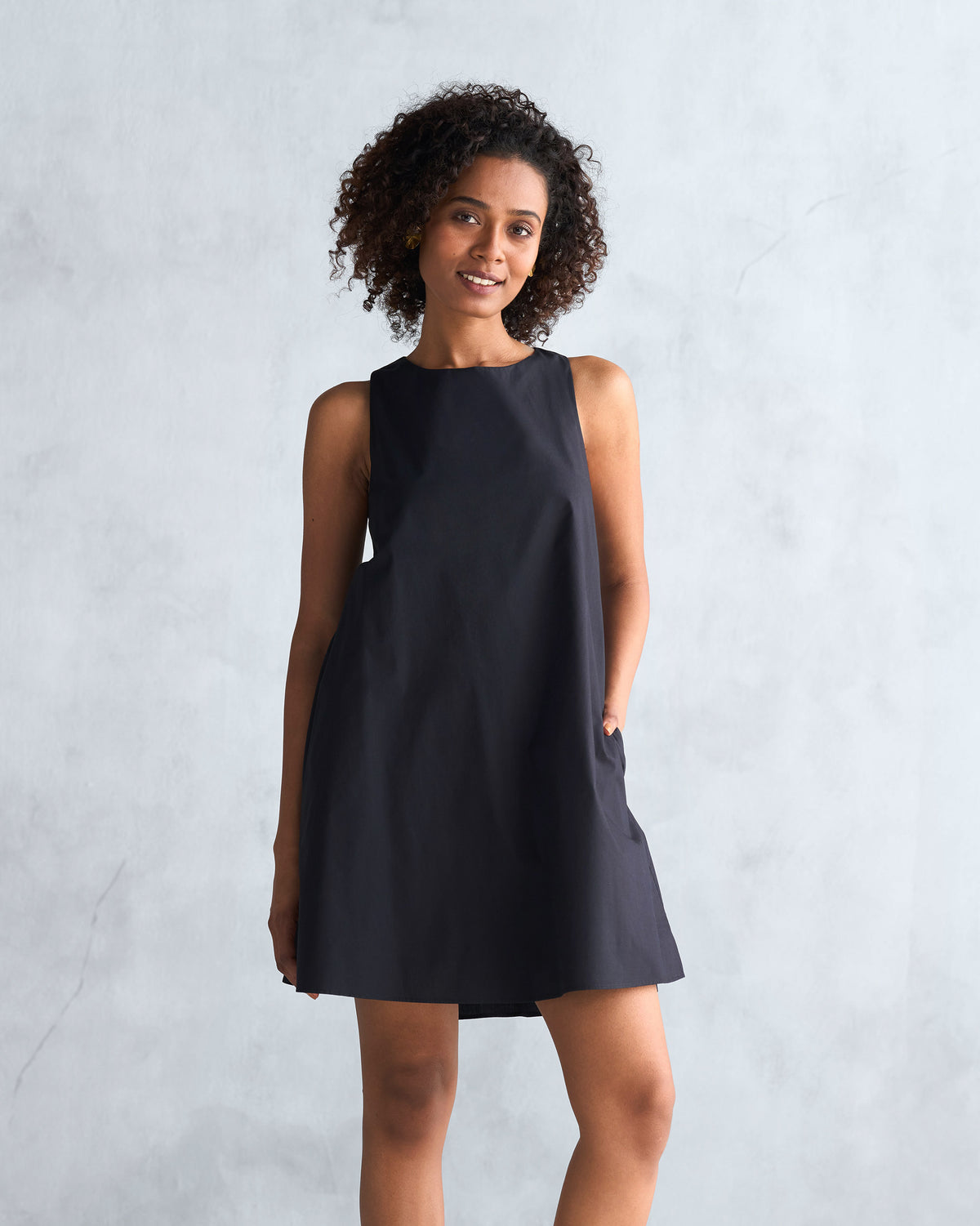 Person wearing a black short racerback dress with a sleeveless A-line shape.