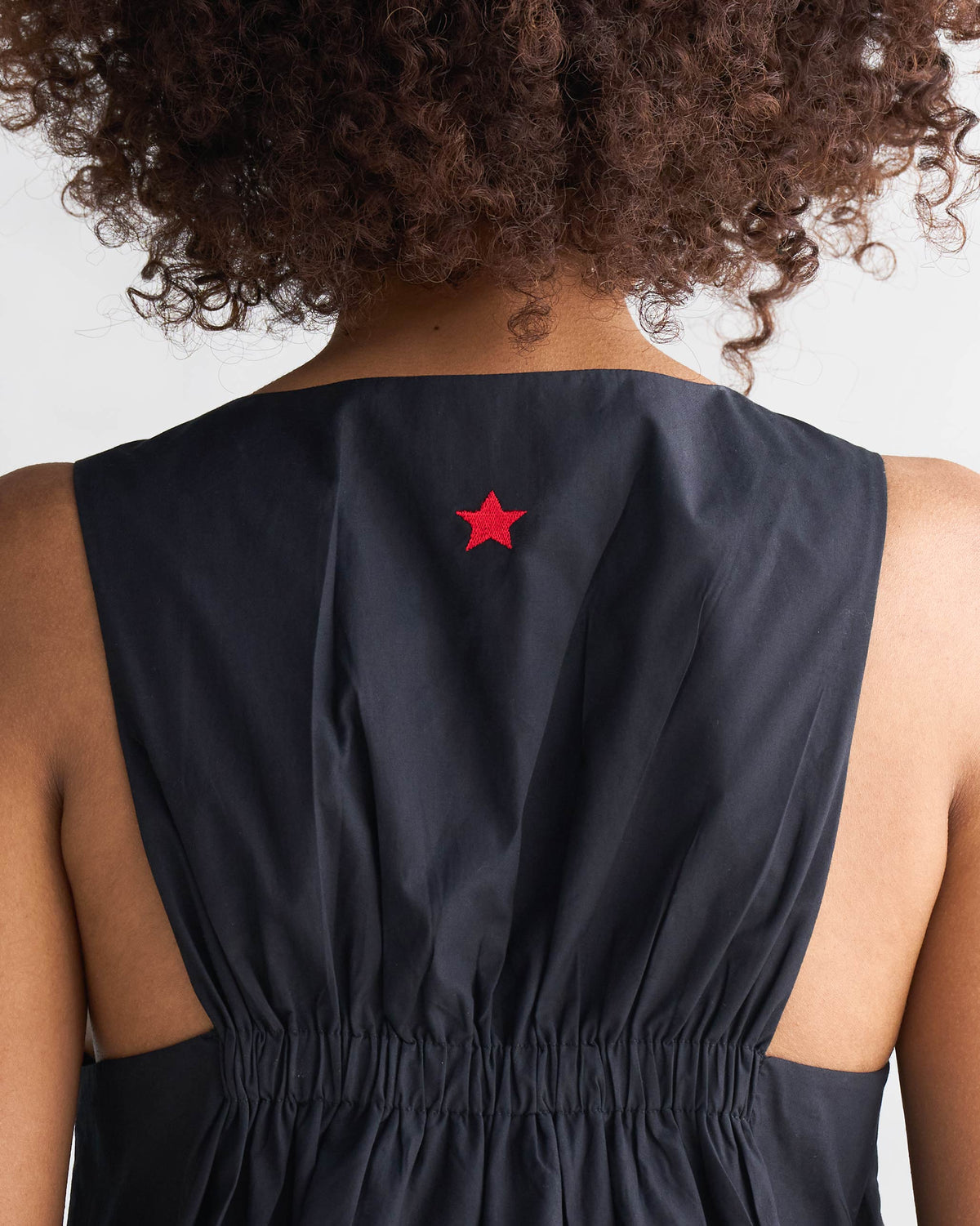 Close-up of a red star on the upper back of a black short racerback dress.