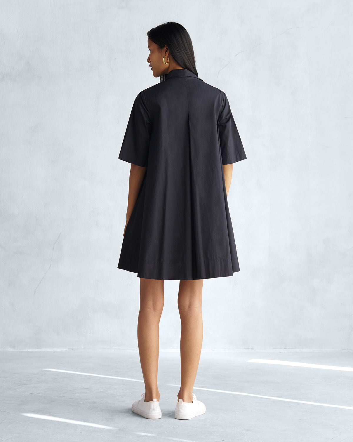 Back of a black A-line short dress with a deep center pleat.