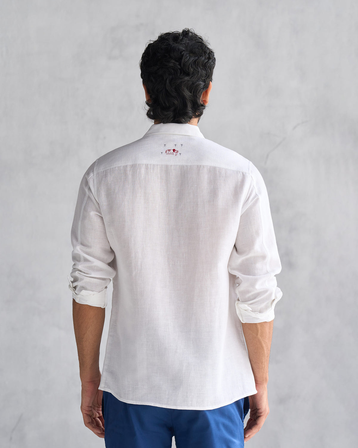 Back of a white August Shirt with sleeves rolled, worn by a person.