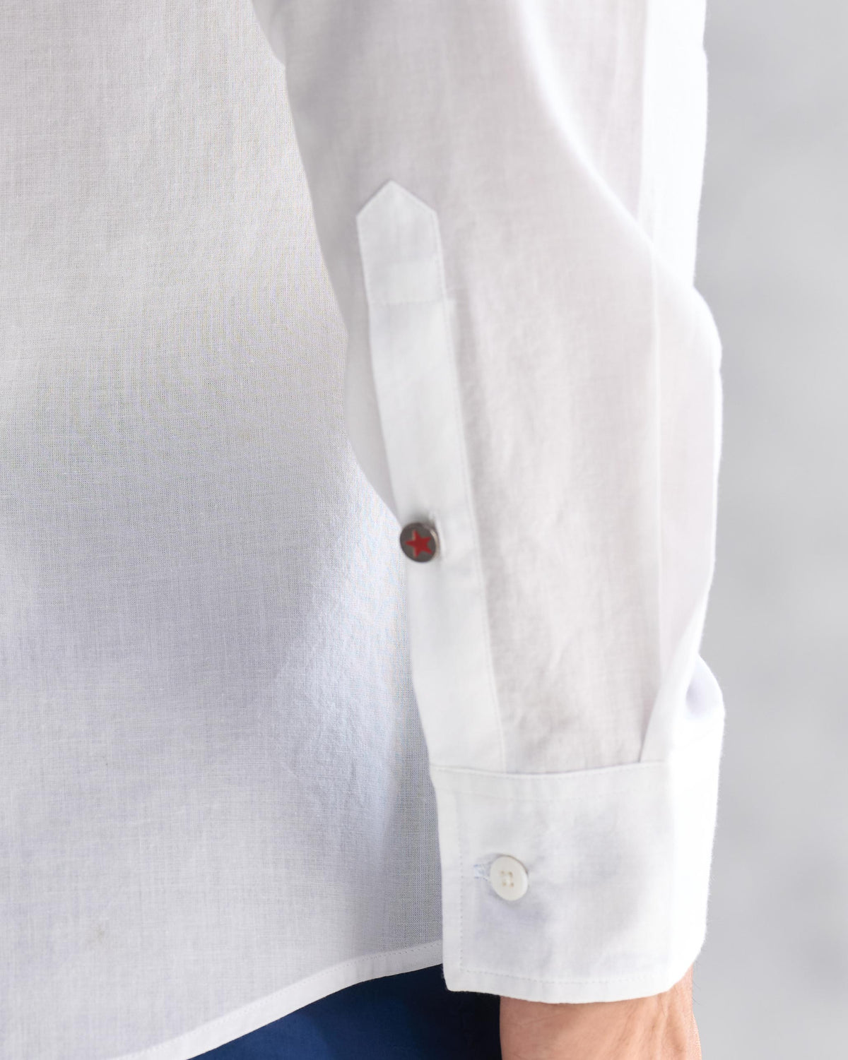 Close-up of a white Classic shirt sleeve with a red star button on the placket.
