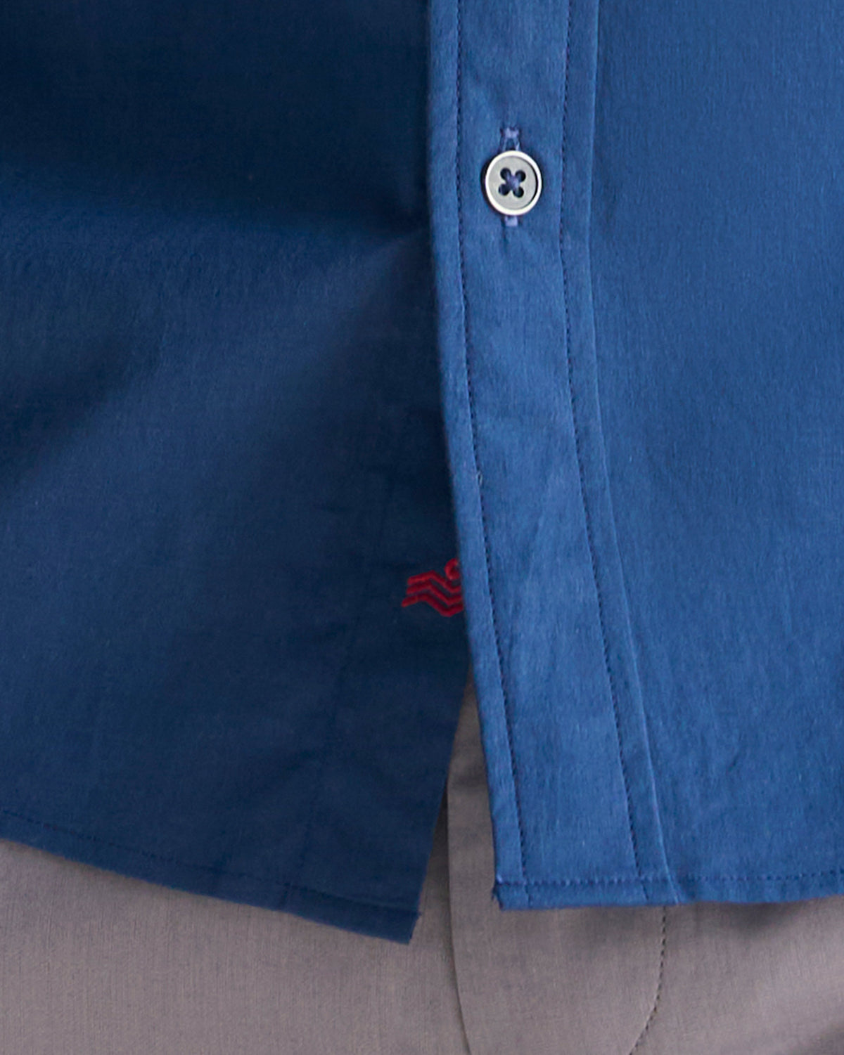 Close-up of a navy Classic Shirt placket with a small red embroidered logo near the hem.