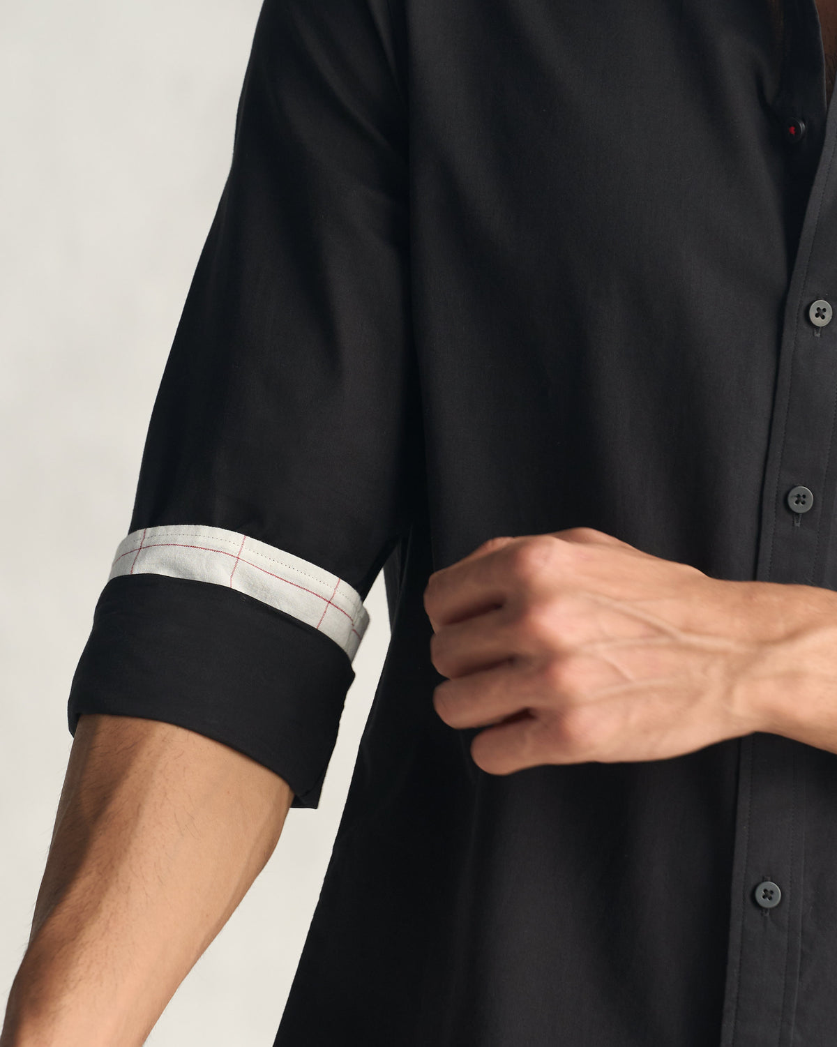 Rolled black shirt sleeve showing a windowpane check cuff lining.