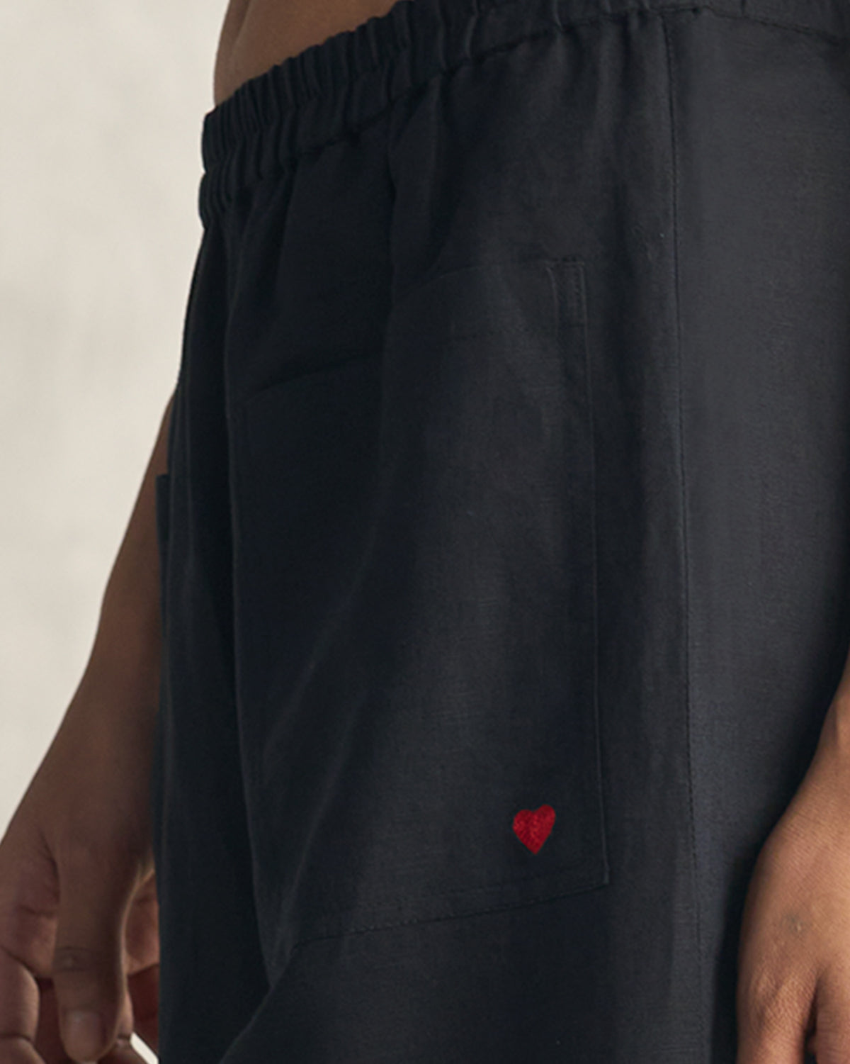 Close-up of a red heart embroidered on the pocket of black Serene pants.