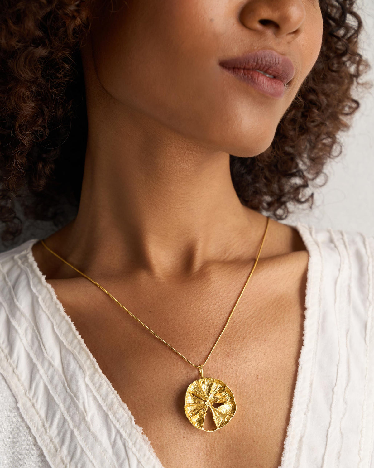 Gold lemon slice charm on a fine chain at the collarbone.