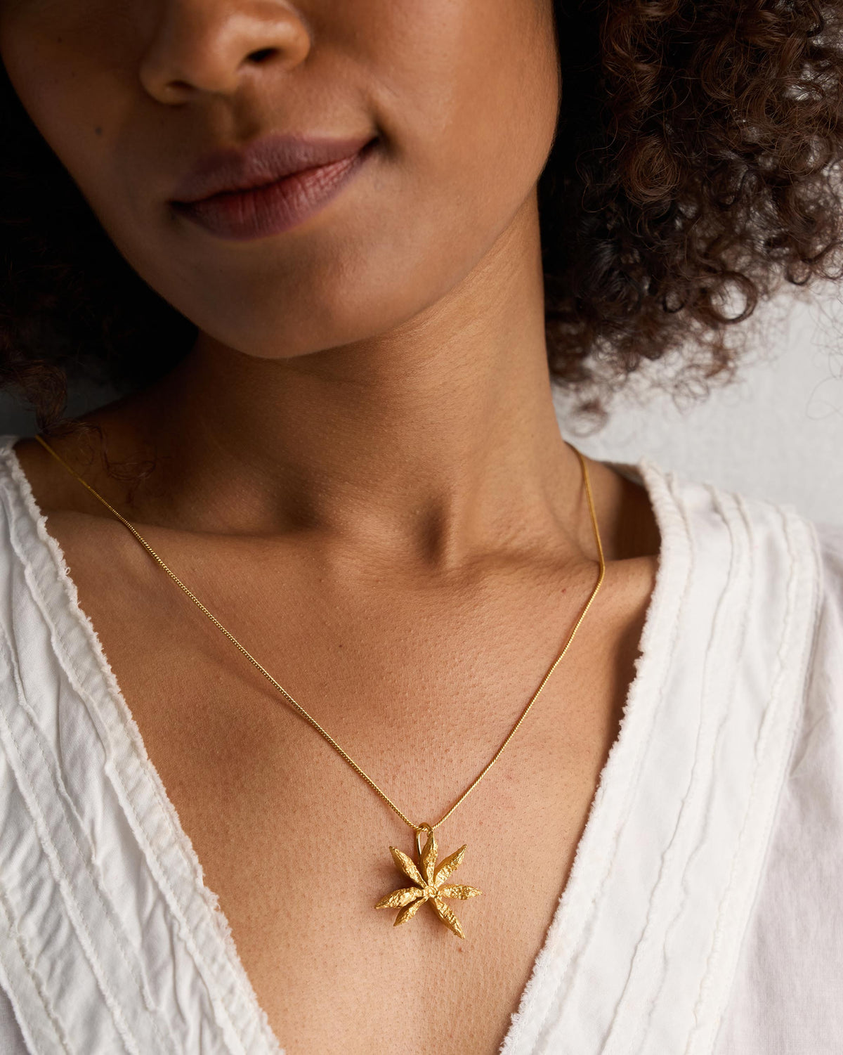 Person wearing a large gold Star Anise charm pendant.