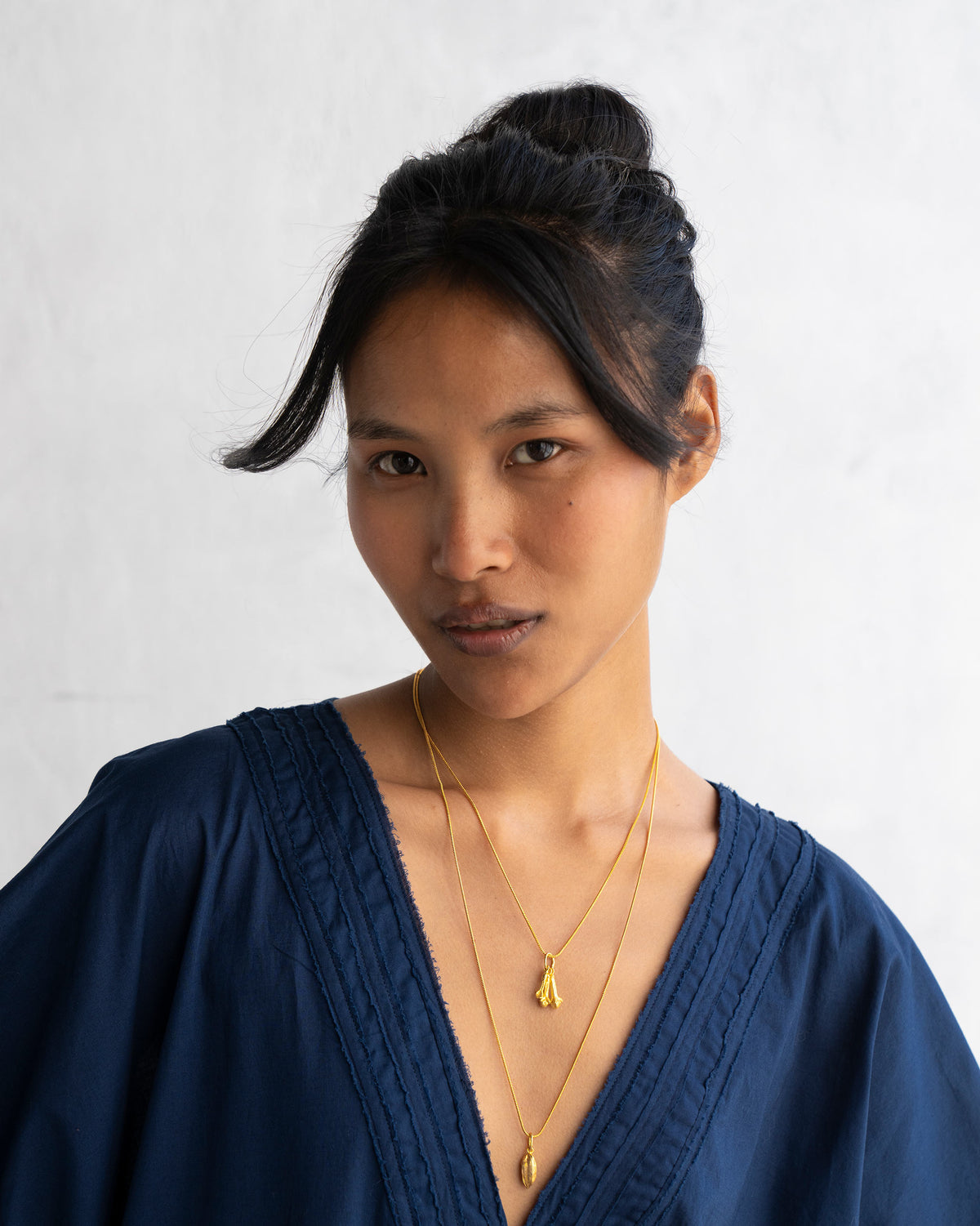 Small gold Cardamom charms worn on layered gold chains.