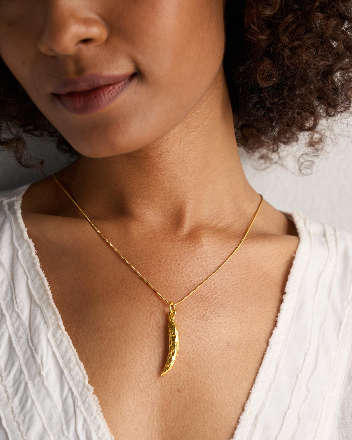 Gold chilli charm on a fine chain at the collarbone.
