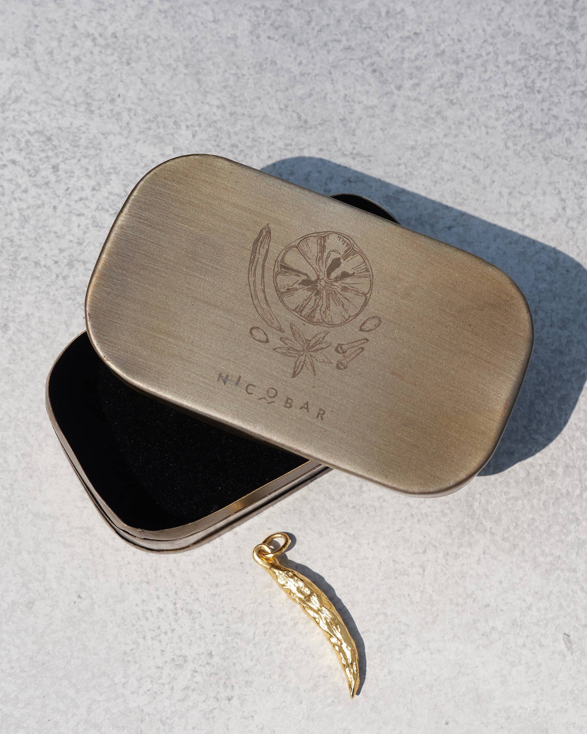Gold chilli charm beside its Nicobar spice-illustrated gift tin.
