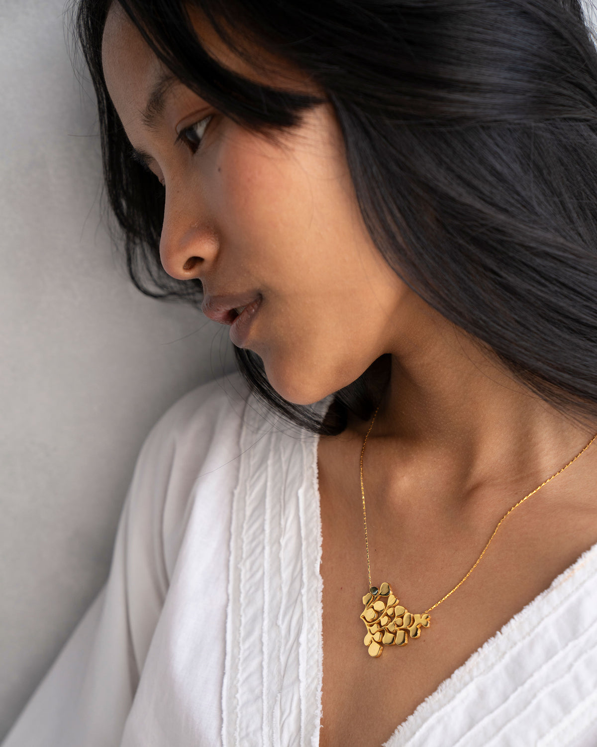 Person wearing a gold Fern Necklace with a textured leaf pendant.
