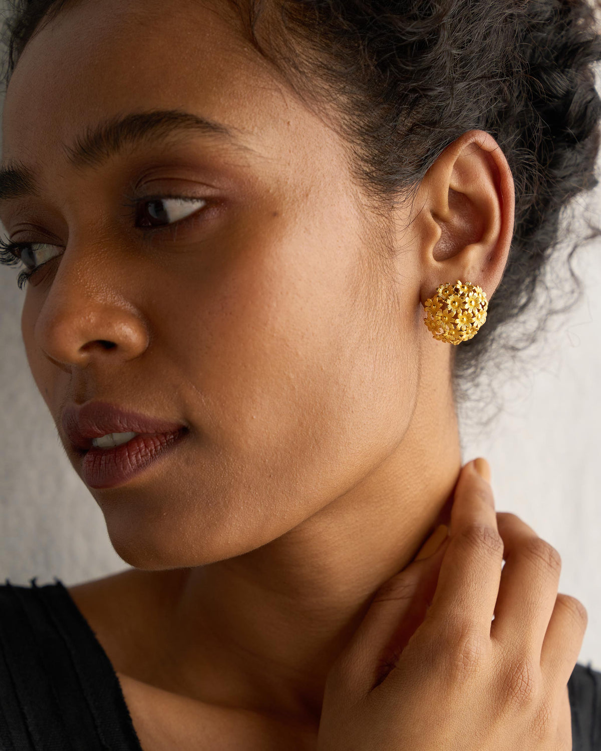 Close-up of gold Rhododenron earring worn on an ear, showing its textured dome shape.