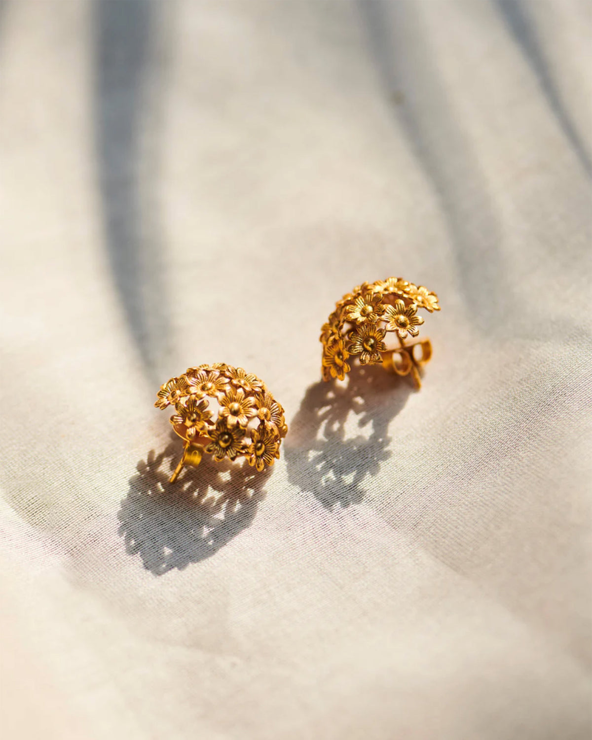 Pair of gold Rhododenron earrings with a cluster of small flowers, laid flat.