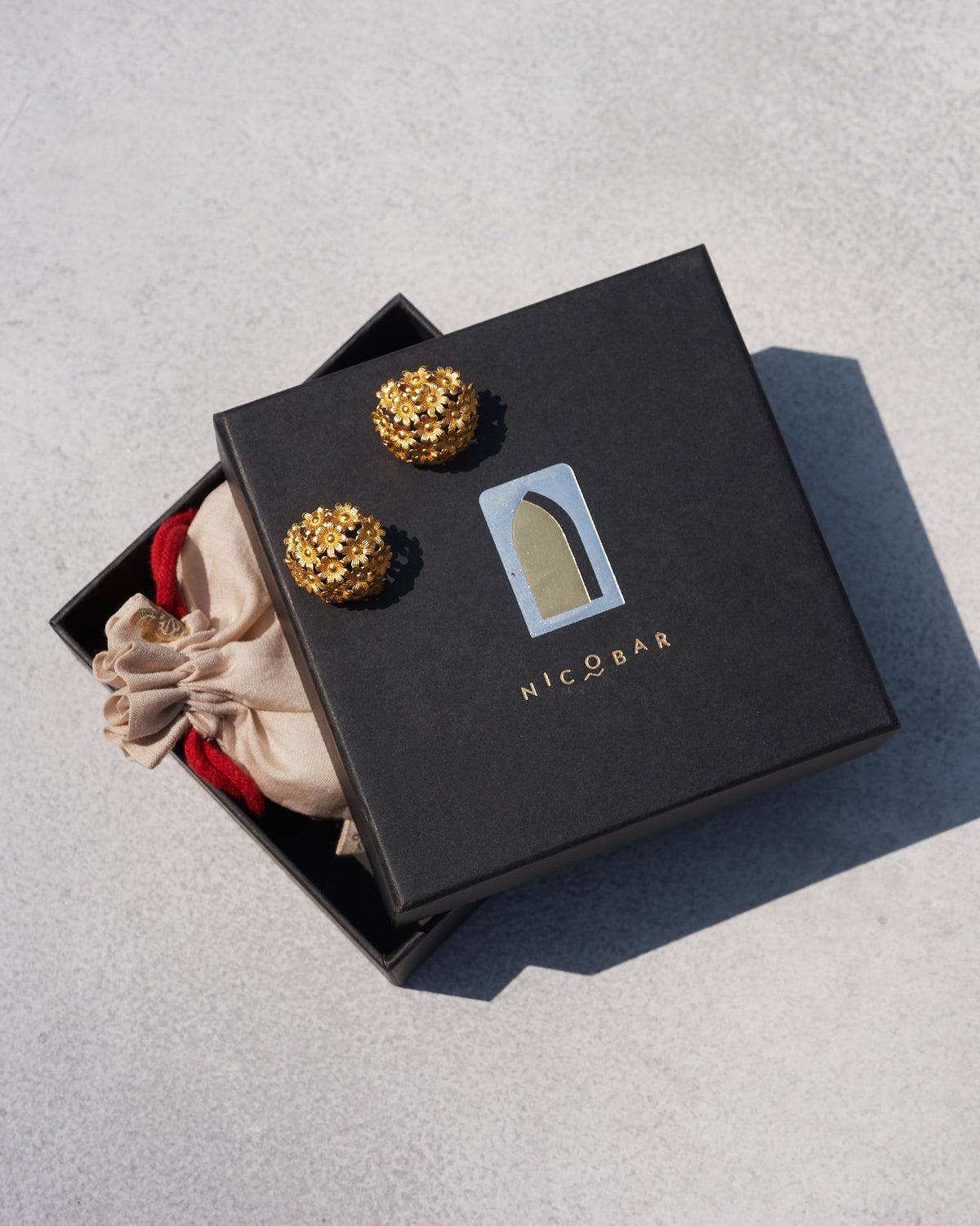 Pair of gold Rhododenron earrings displayed on a Nicobar gift box.
