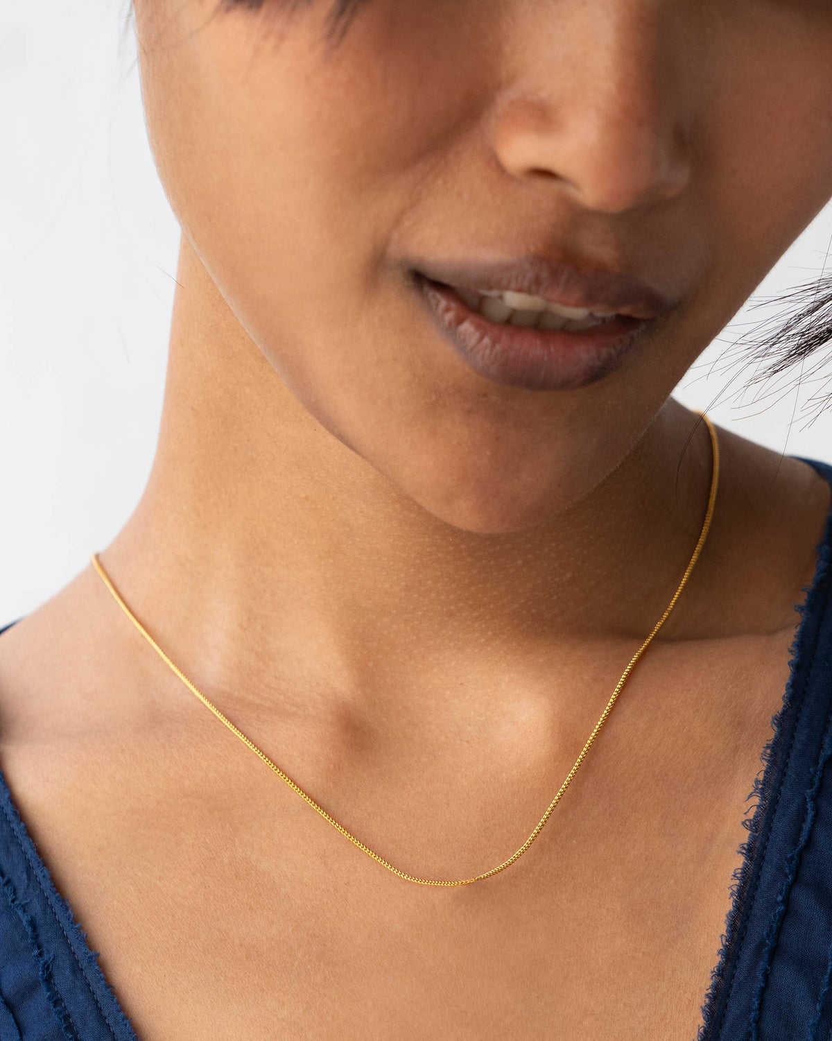 Fine gold snake chain worn at collarbone length.