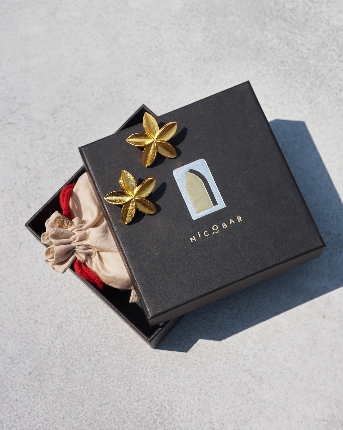Pair of gold Frangi Studs resting on a Nicobar gift box.