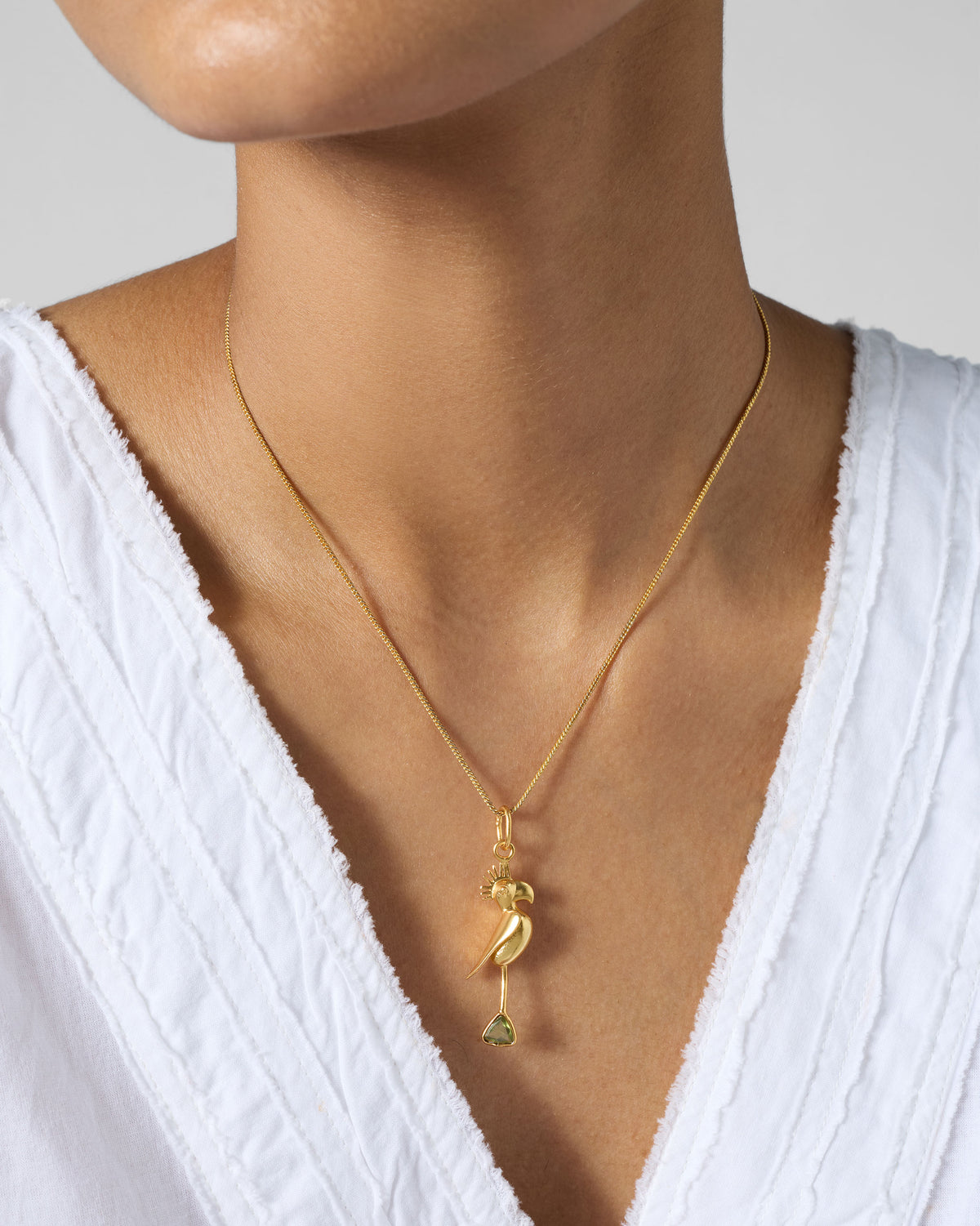 Person wearing a gold Parrot Charm on a fine chain, with a green drop.