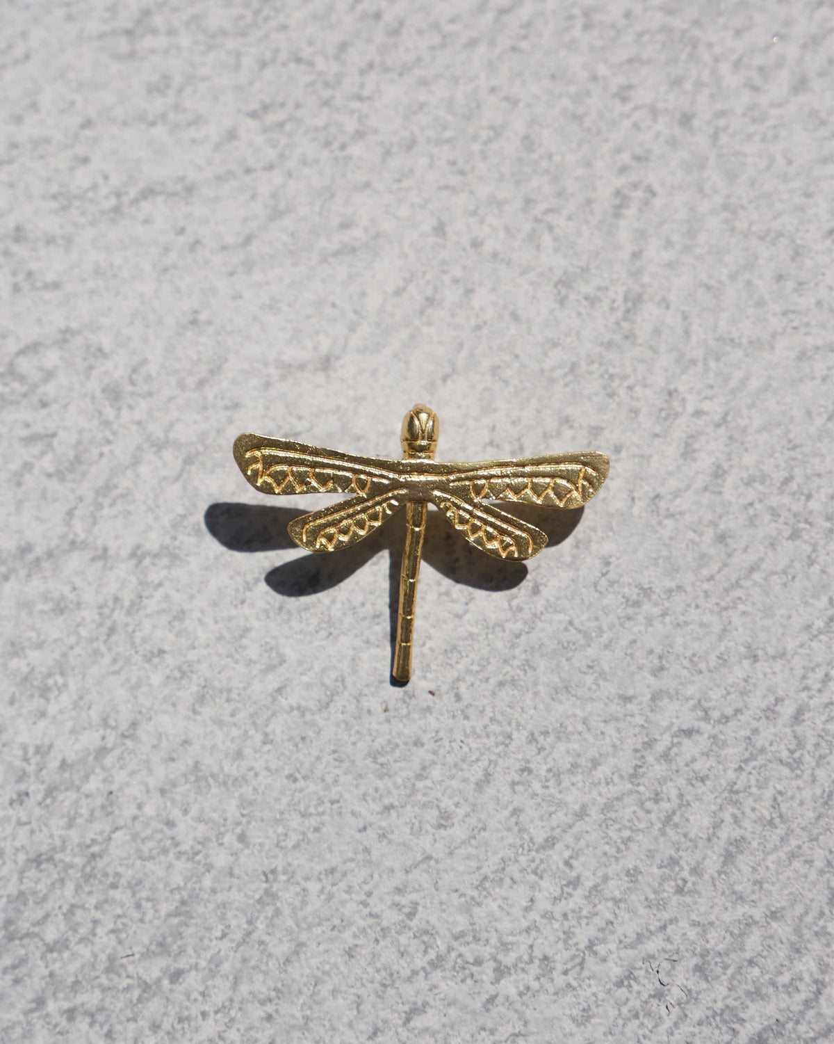 Close-up of a gold Dragonfly Charm showing its patterned wings.