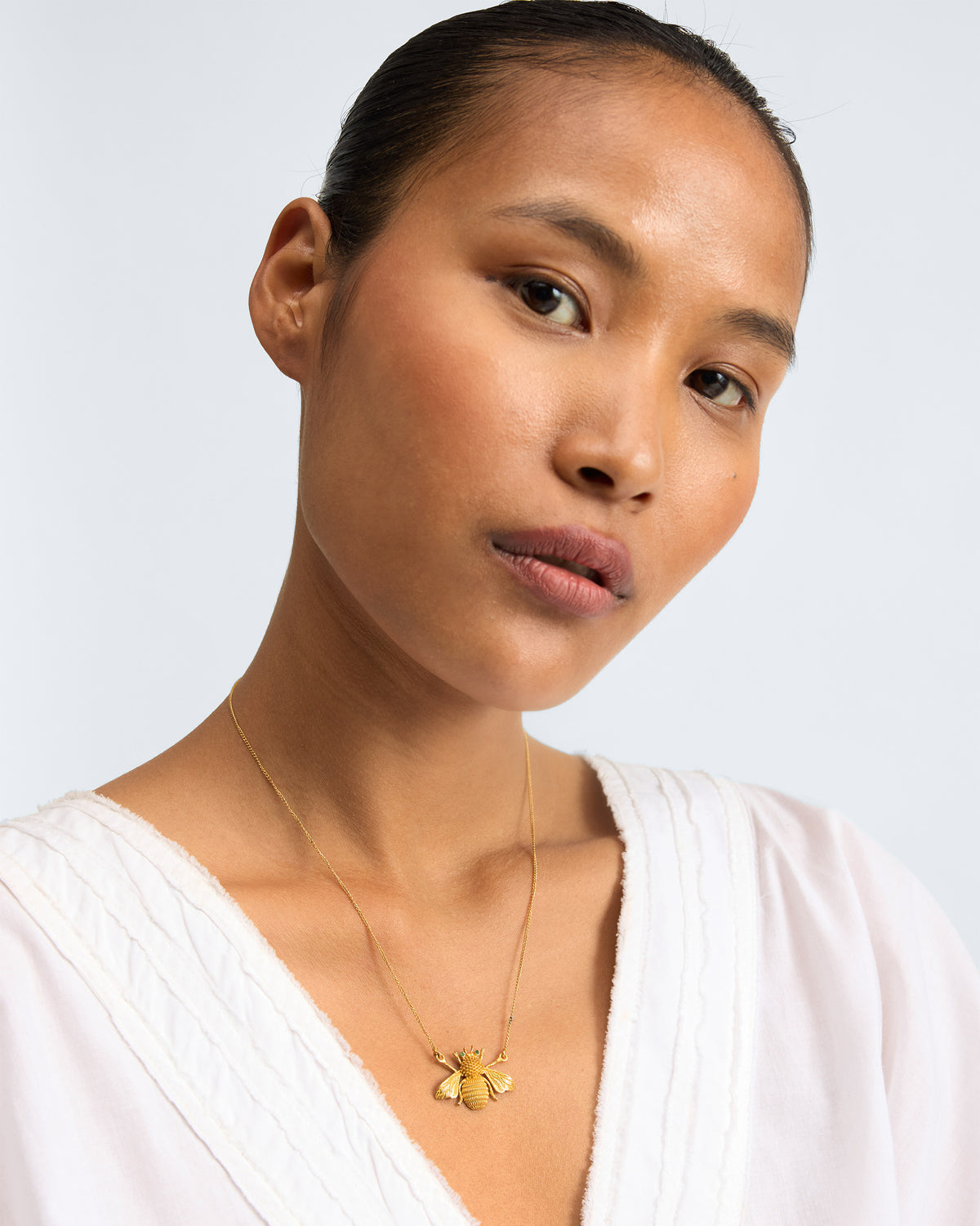 Person wearing Bee Necklace with a small gold bee pendant near the neckline.