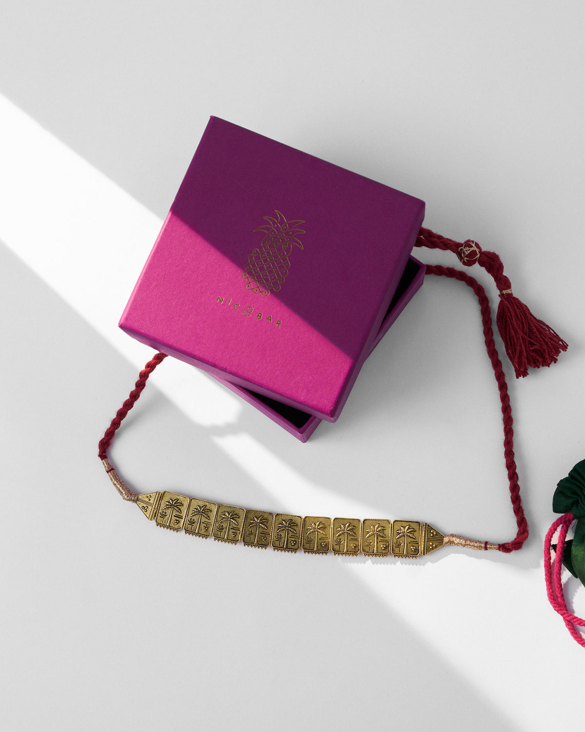 Antique gold coco palm necklace beside a magenta Nicobar gift box.