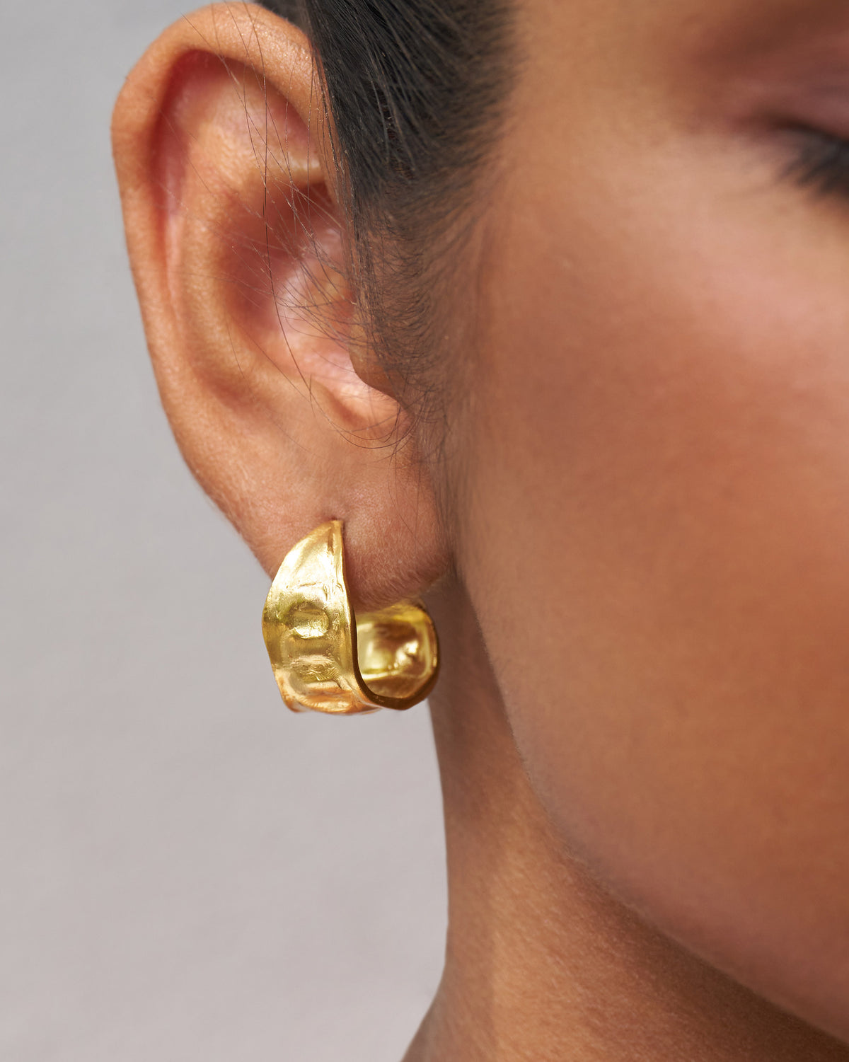 Close-up of gold Seed Pod Small Hoops worn on an ear, showing the textured surface.