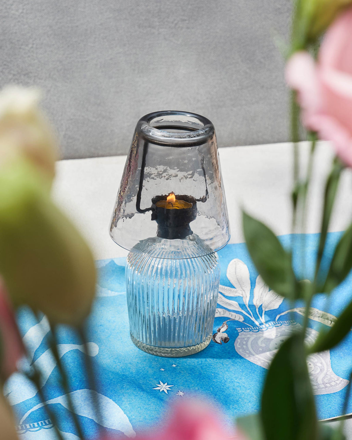 Lit Asfar votive with a clear ribbed base and smoky grey glass shade.