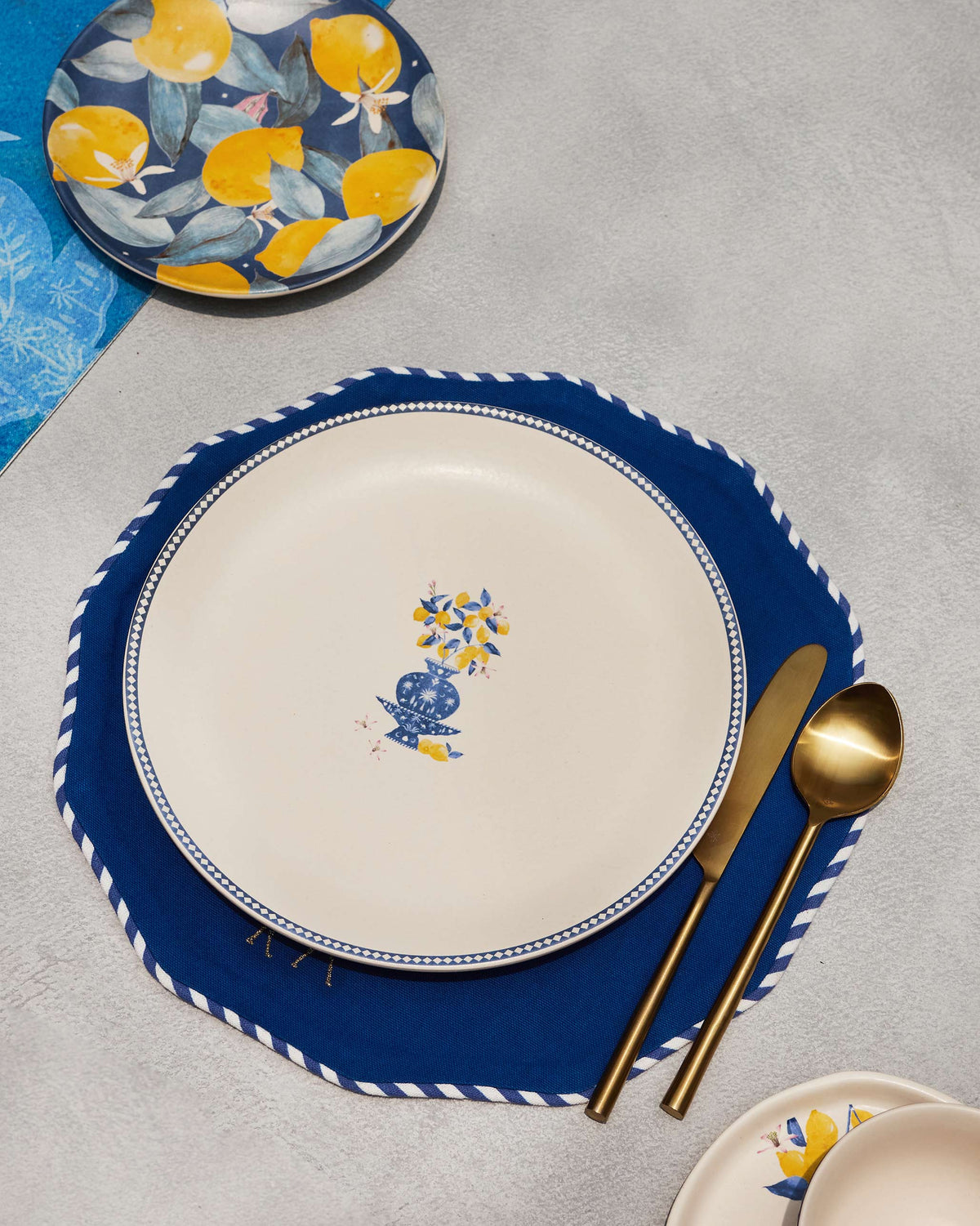 Sahara dinner plate with lemon vase motif set on a navy placemat with gold cutlery.