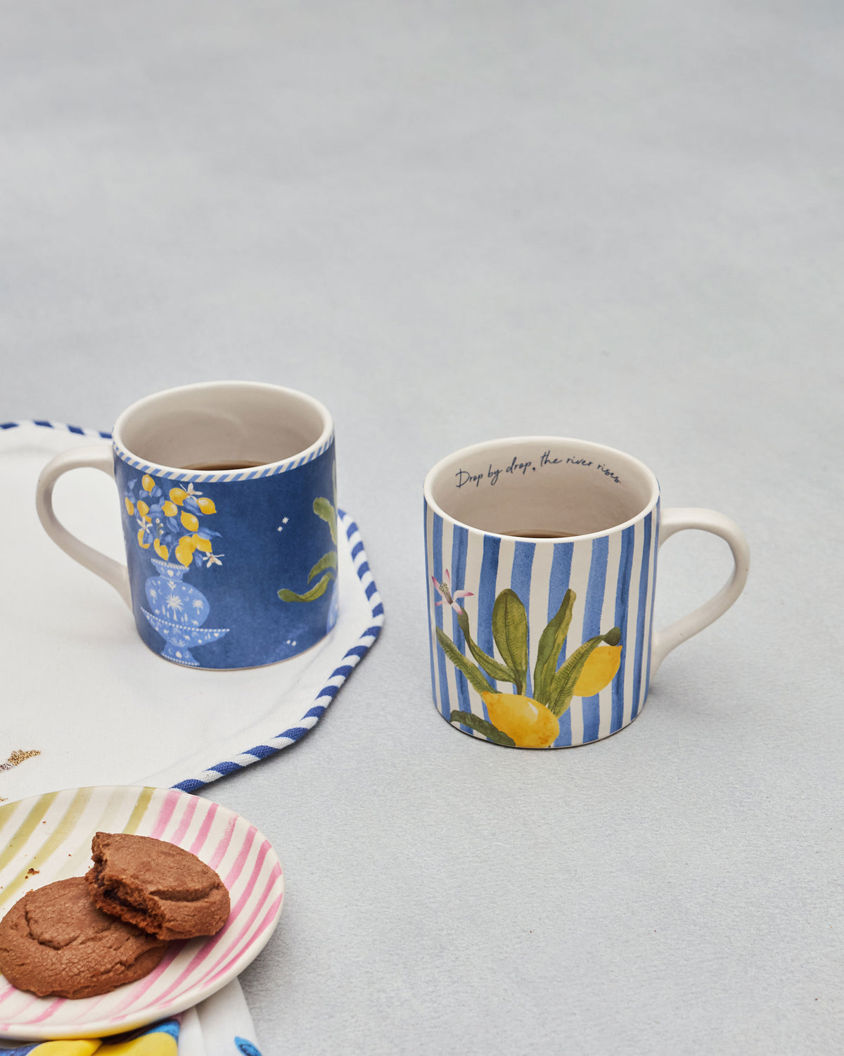 Asfar lemon mugs filled with coffee beside cookies on a striped saucer.