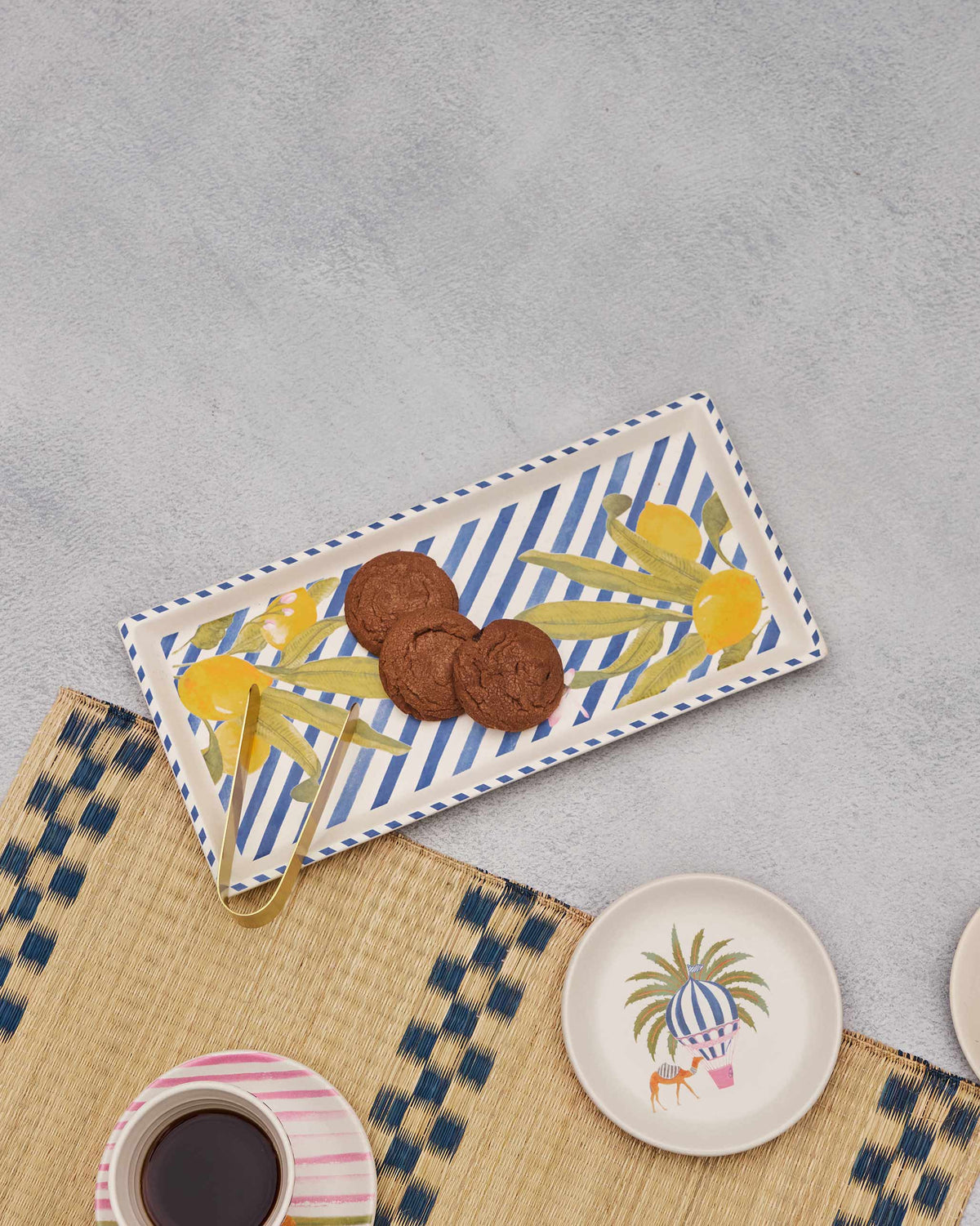 Asfar cookie tray serving chocolate cookies with gold tongs on a woven mat.