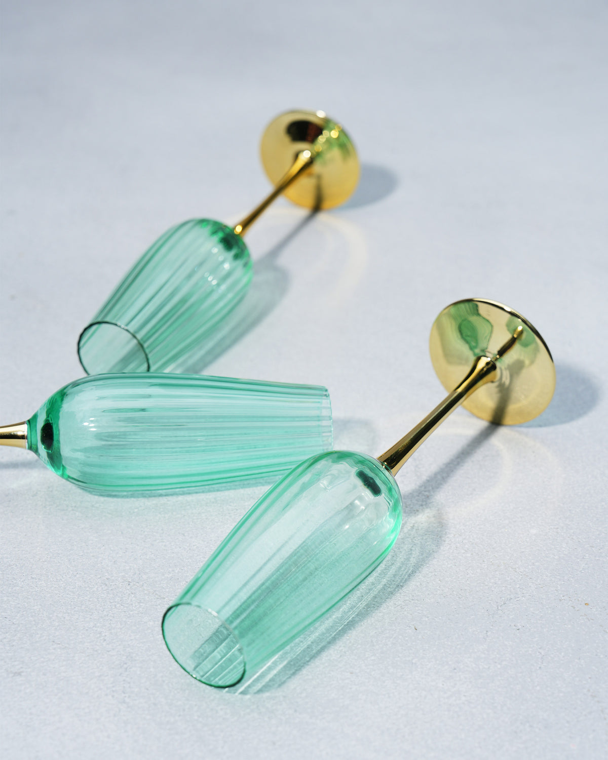 Three seafoam green champagne flutes lying on a grey surface.