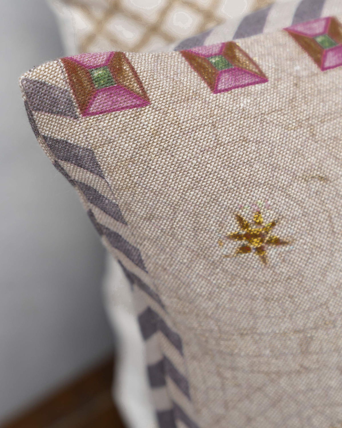 Close-up of Chambray Arch Cushion showing pink diamond motifs and a grey striped edge.