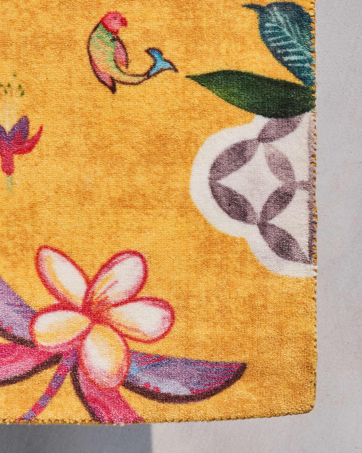Close-up of a yellow Mandovi rug corner showing a flower and leaf motif.