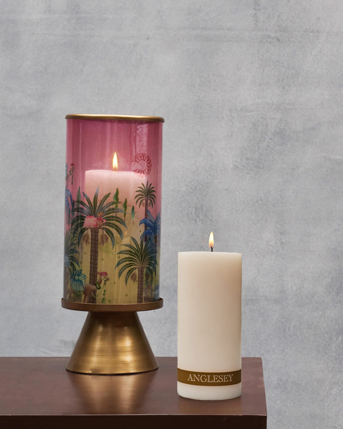Lit Anglesey Pillar Candle beside a candle holder on a wooden shelf.