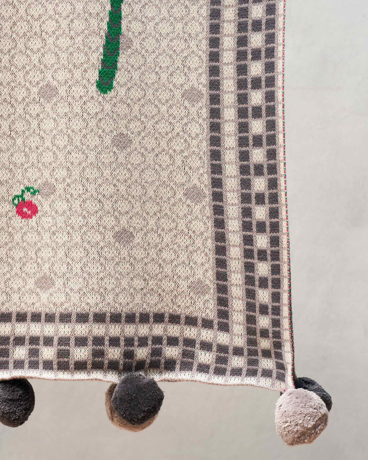 Close-up of the Mirage throw edge showing its checked border and pom-poms.