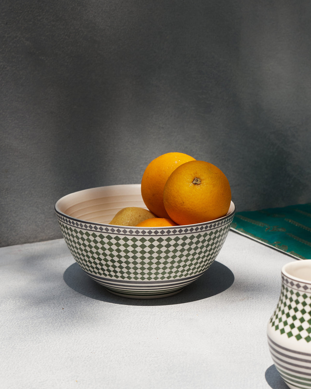 Zellij Serving Bowl filled with oranges and kiwi on a grey table.
