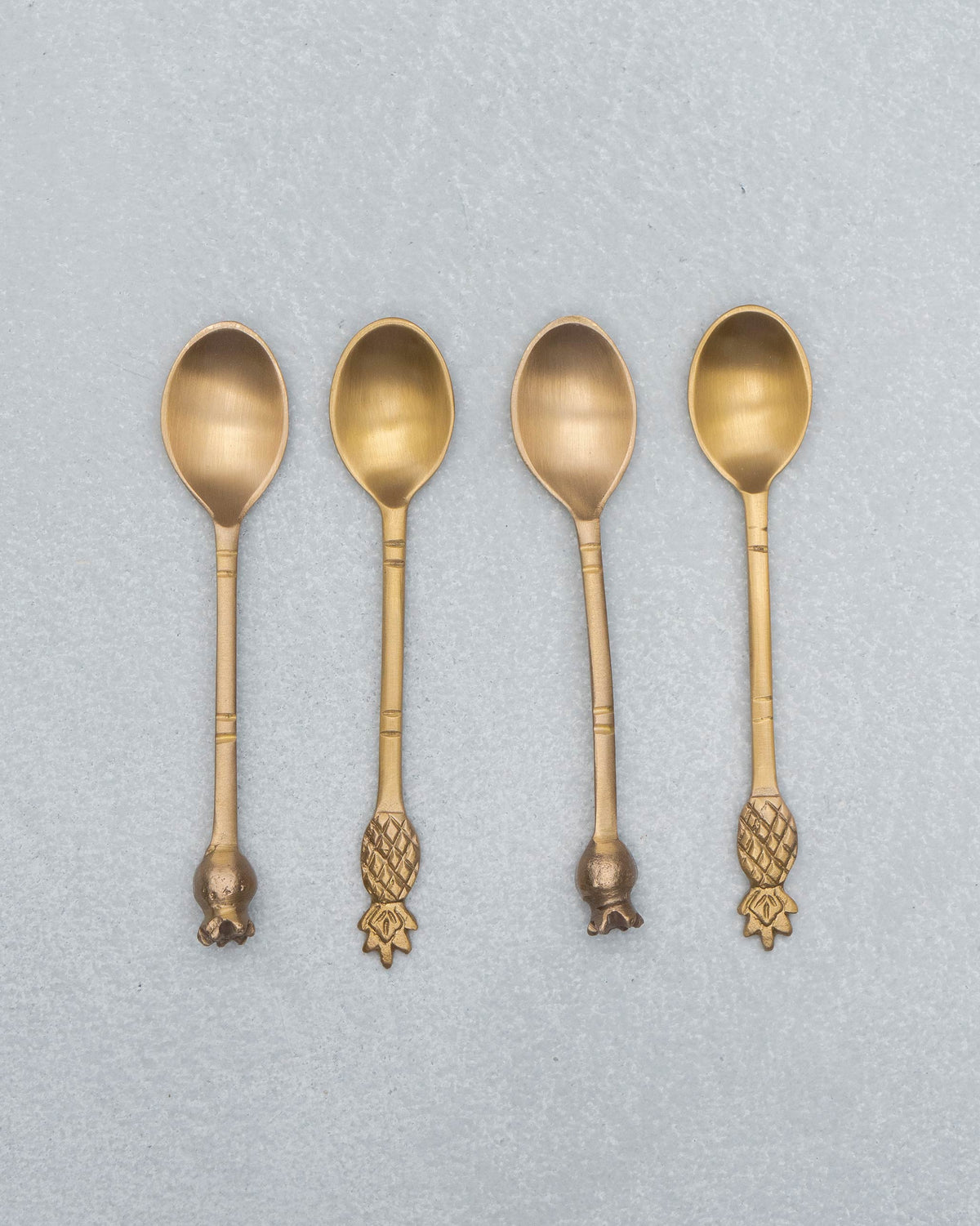 Four brass Dune coffee spoons with pineapple and pomegranate finials.