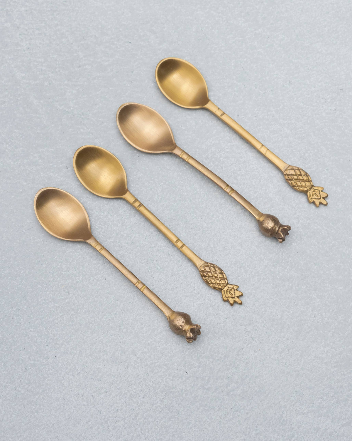 Four brass Dune coffee spoons laid diagonally showing fruit finials.