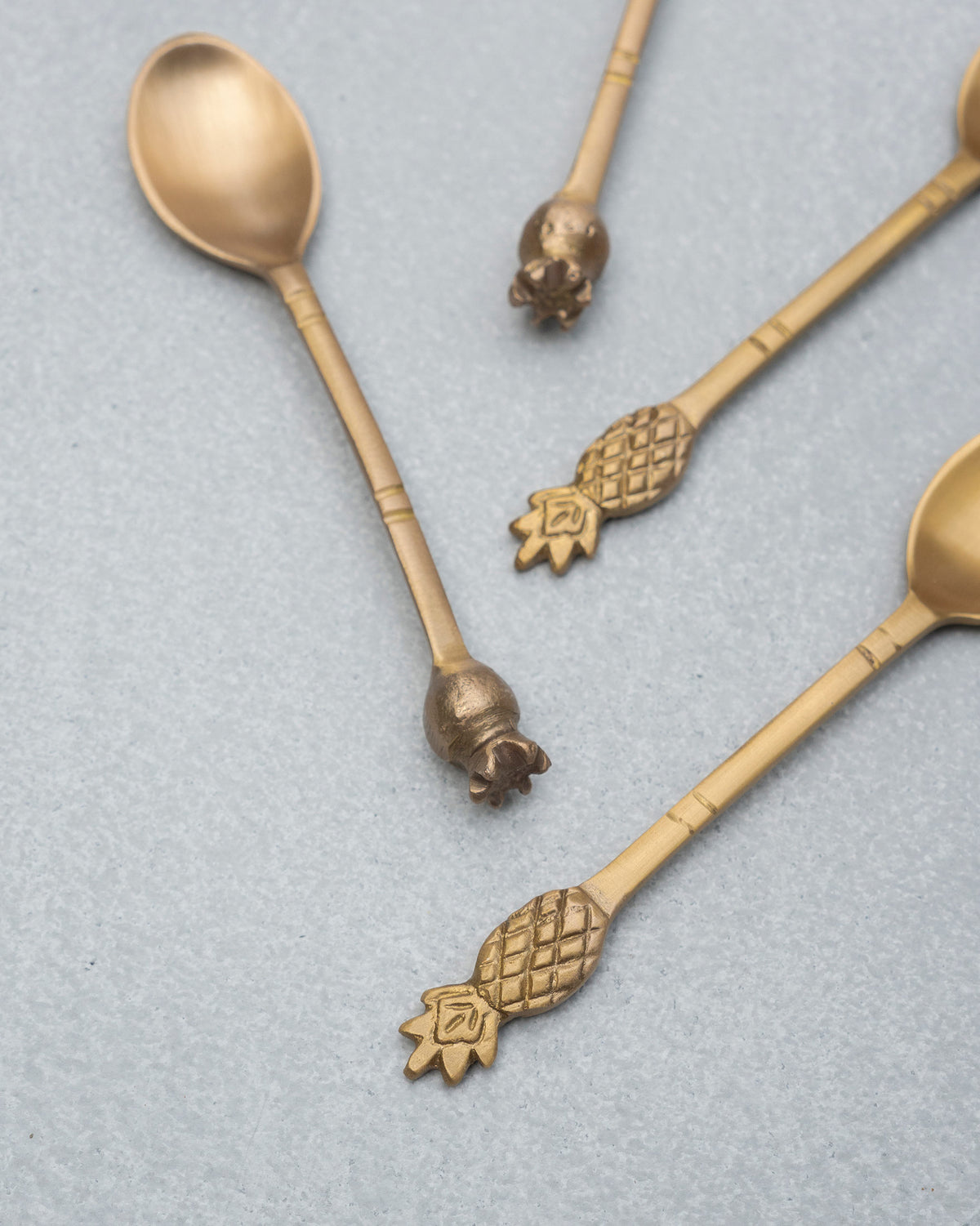 Close-up of pineapple and pomegranate finials on brass Dune coffee spoons.
