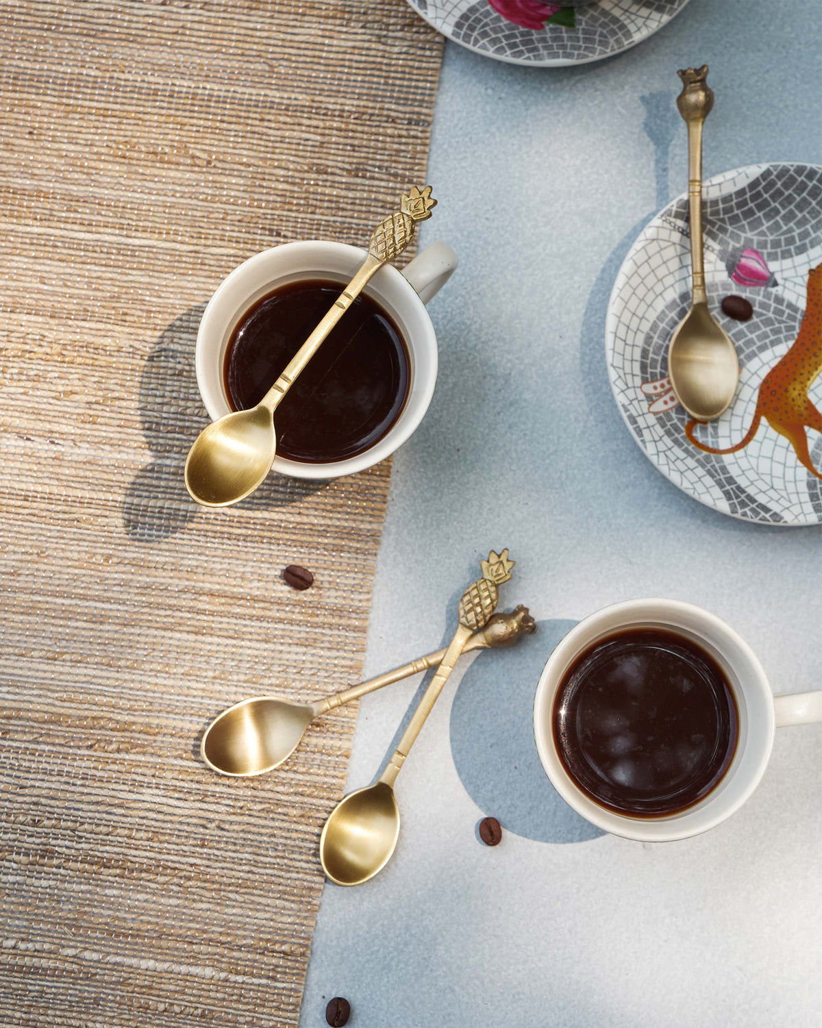 Brass Dune coffee spoons with coffee mugs and scattered beans.