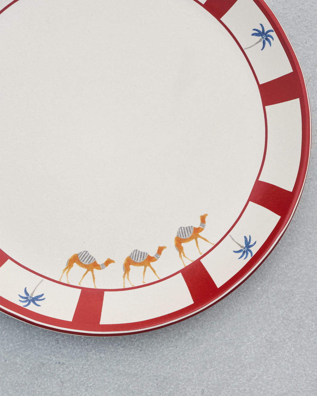 Close-up of Desert Trail Dinner Plate showing a red rim with camels and blue palms.