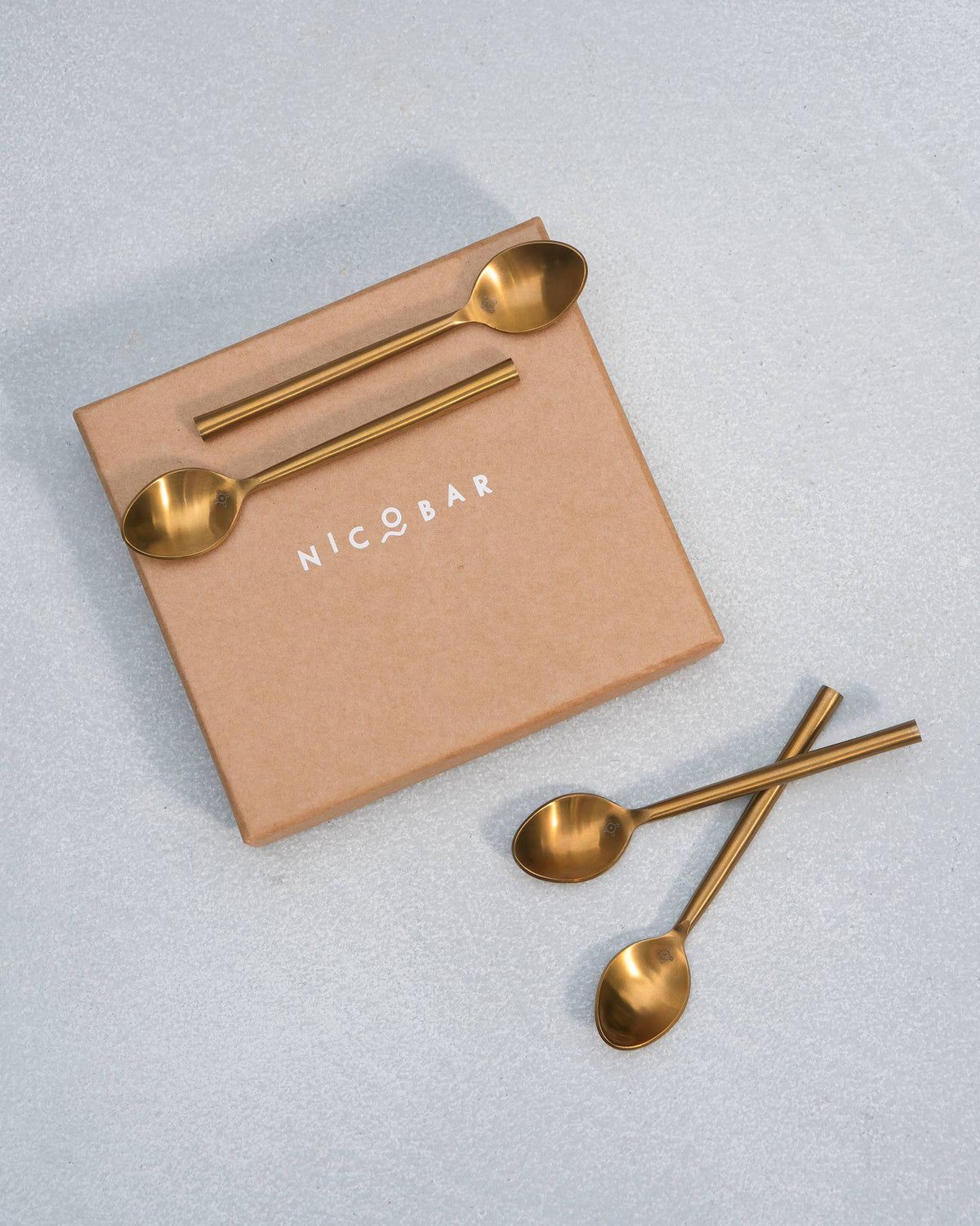 Gold Sahara dessert spoons arranged with a Nicobar kraft gift box.